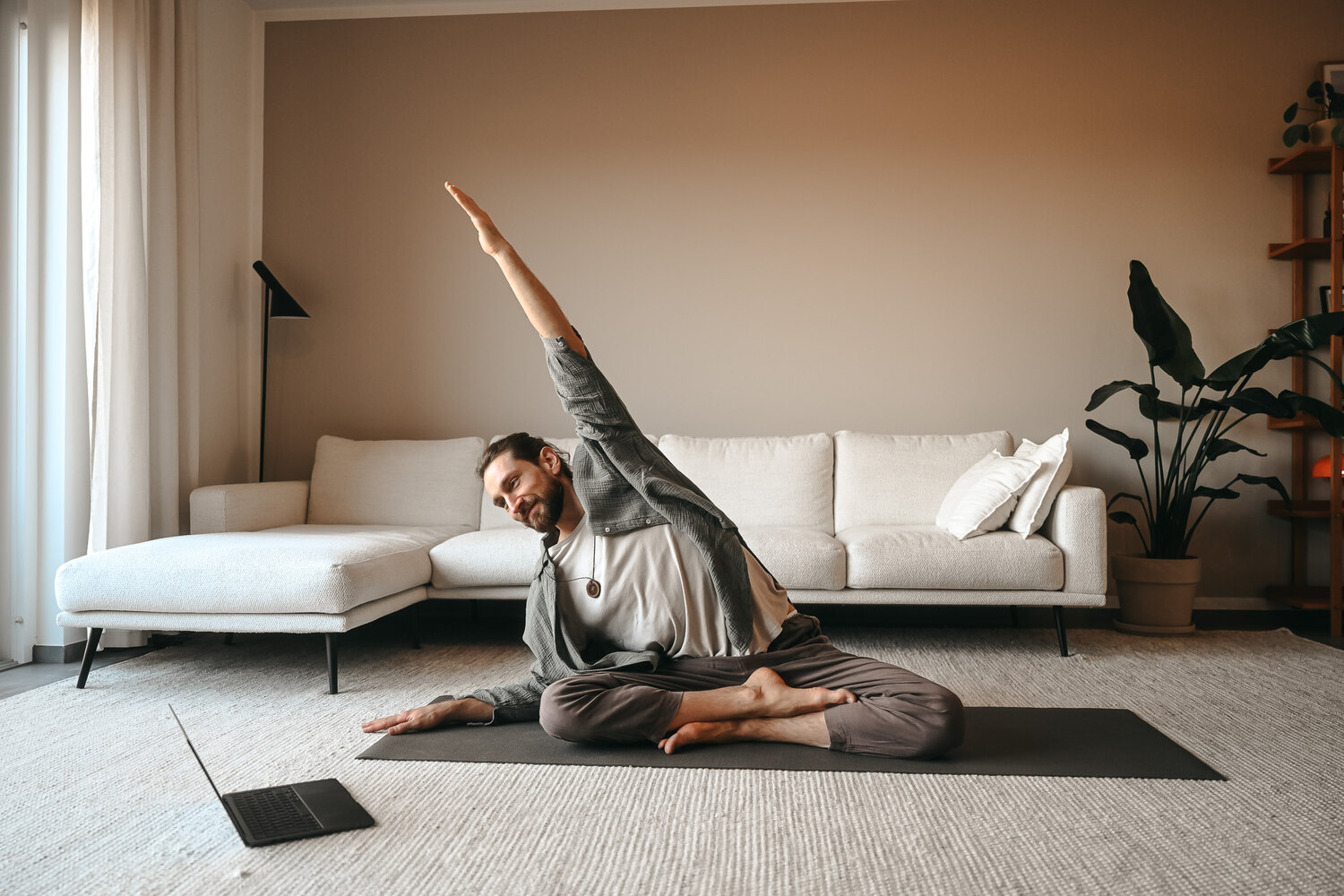 Yogi Igor übt Yoga zu Hause, der Laptop läuft mit